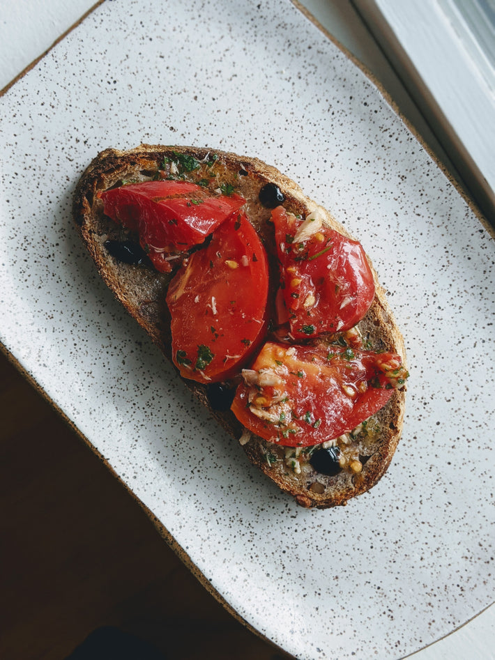 Sourdough toast topped with sliced tomatoes and herbs on a speckled plate