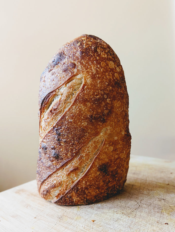 Tall sourdough loaf with golden blistered crust and diagonal scoring, standing on a wooden board.