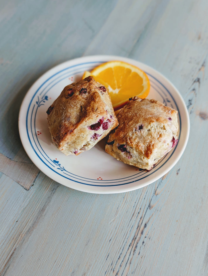Two orange cranberry biscuits on a plate with a slice of orange