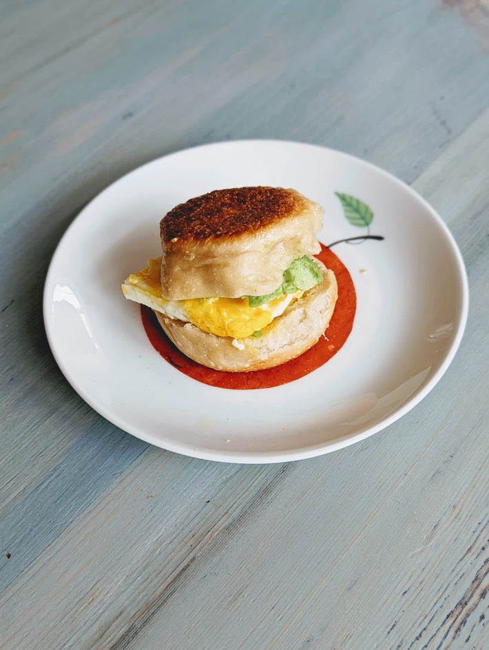 Toasted English muffin sandwich with fried egg and mashed avocado on a white plate