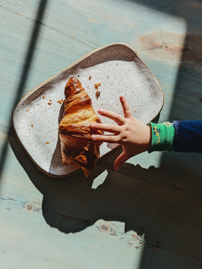 A child's hand reaching for a croissant on a plate