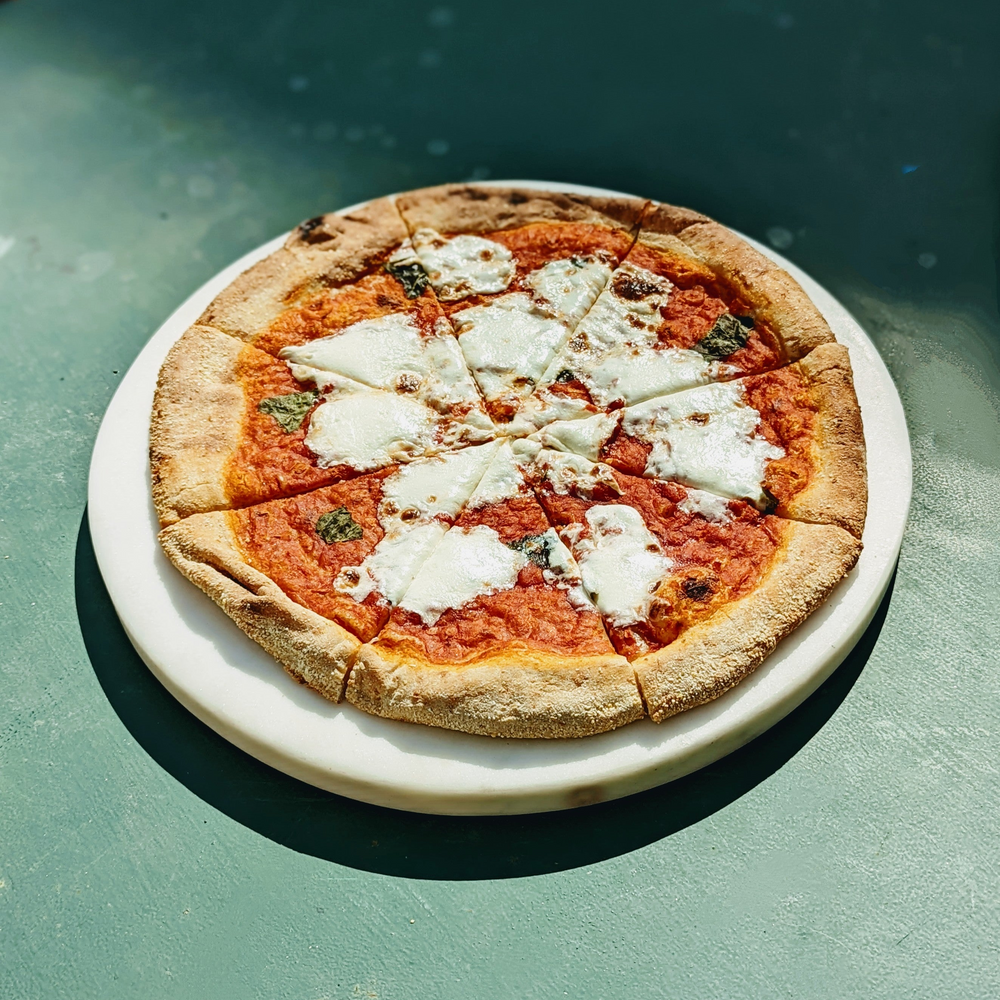Margherita pizza with melted mozzarella and basil on a white marble board, sliced into eight, on a green table