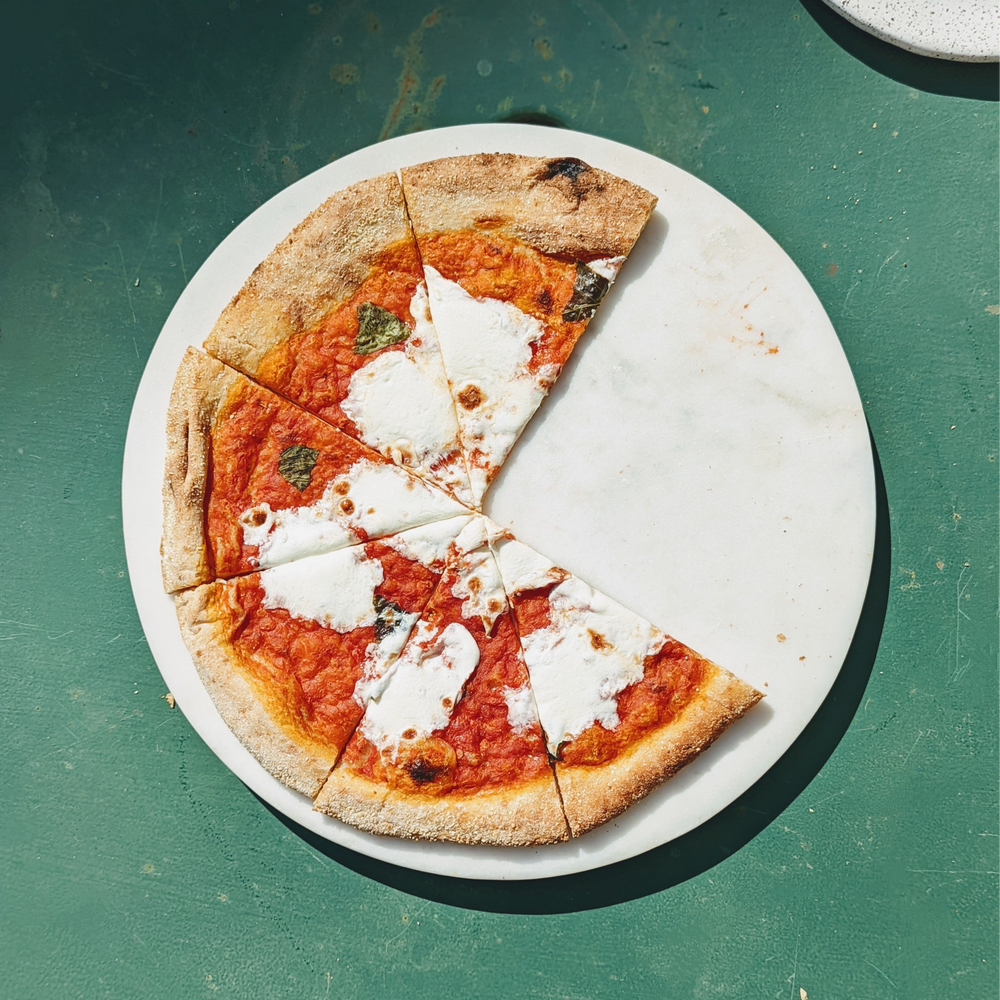 Margherita pizza with four slices remaining on a round marble board over a green table