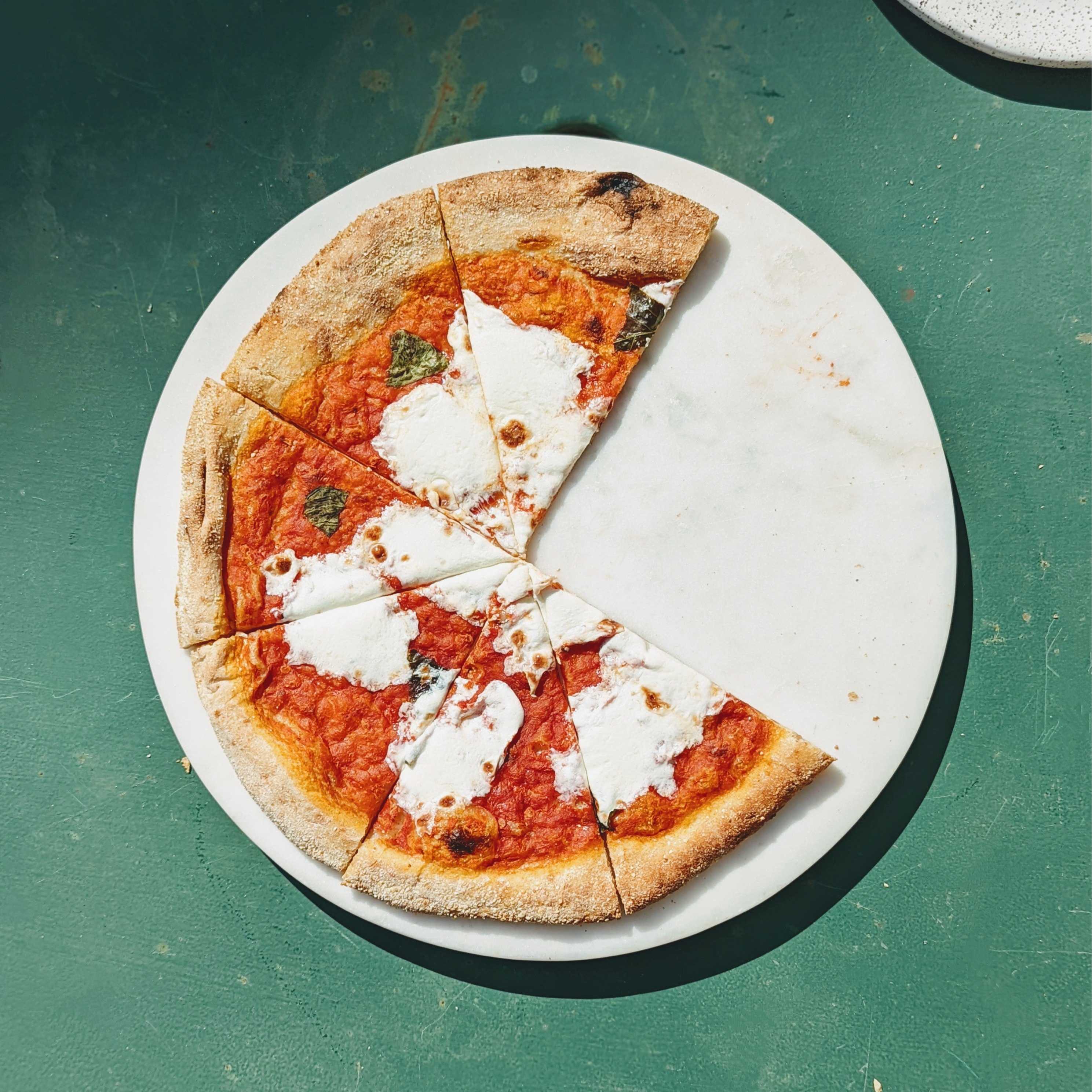 Margherita pizza with four slices remaining on a round marble board over a green table