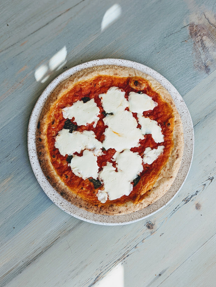 Neapolitan-style margherita pizza with torn fresh mozzarella and basil, top-down on a speckled plate
