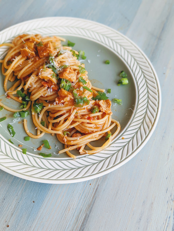 Fresh Tonnarelli pasta topped with sauce and herbs on a plate