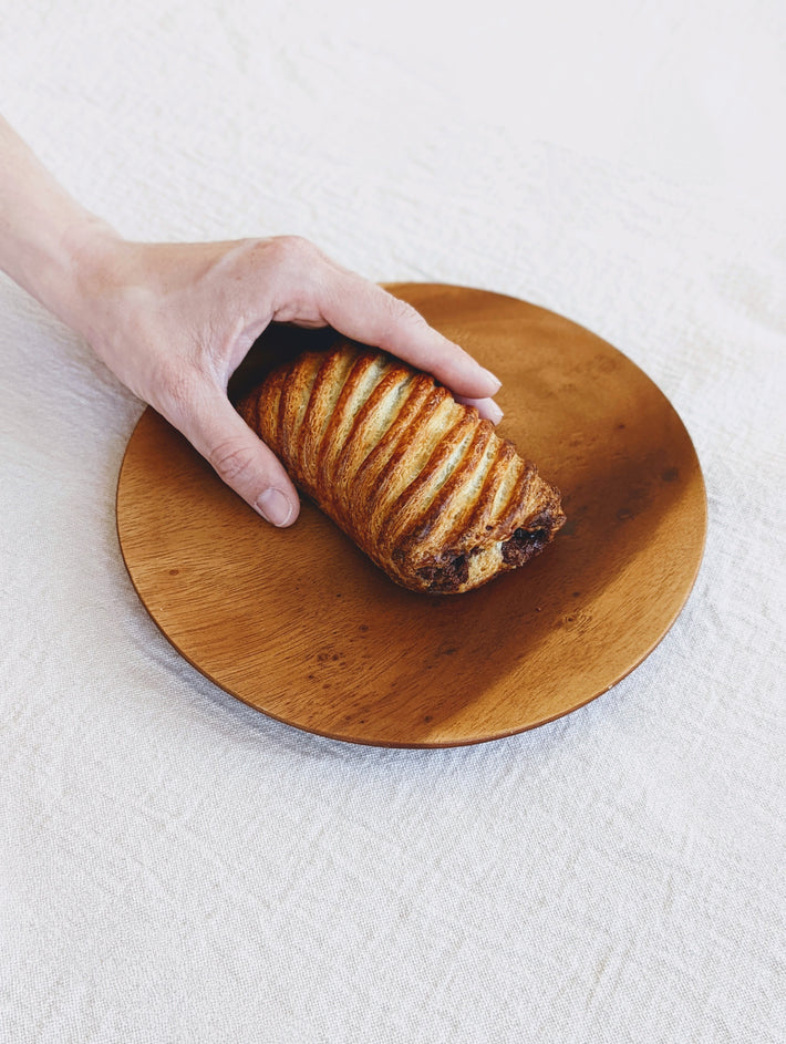 Chocolate Avalanche Croissant on a wooden plate, held by a hand