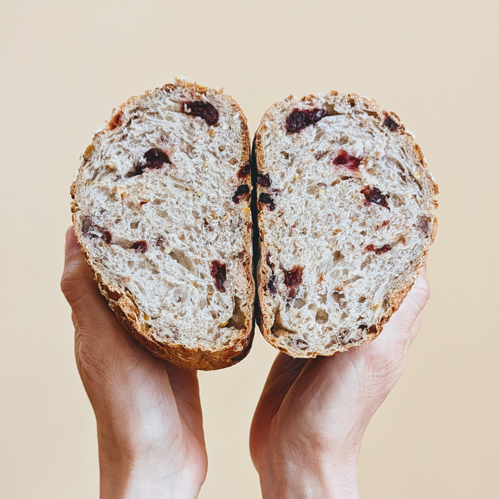 Hands holding two halves of a seeded loaf with visible dried cranberries and open crumb