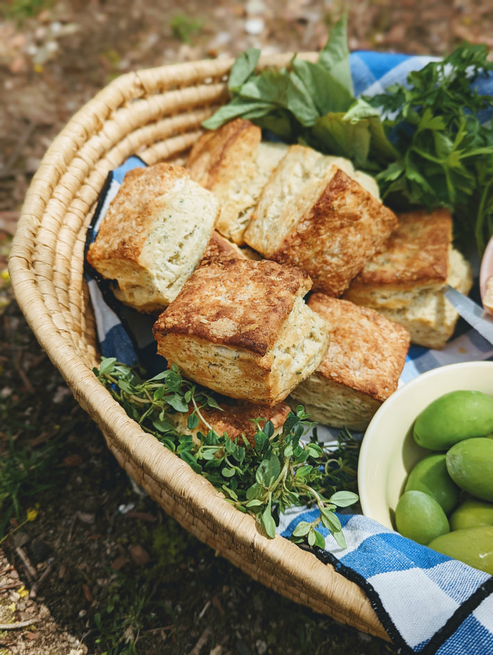 A basket of Parmesan Herb Biscuits with fresh herbs and olives