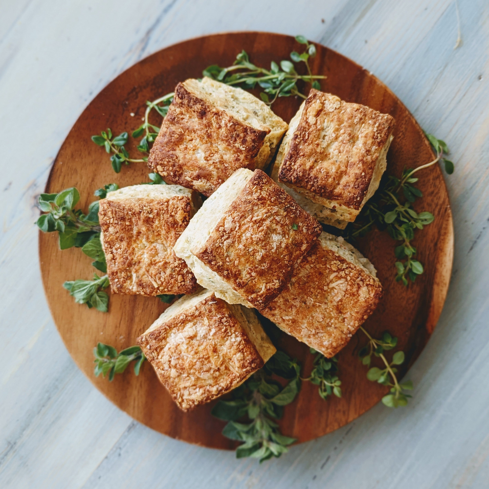 Stack of six square cheddar biscuits on a round wooden board garnished with fresh thyme sprigs