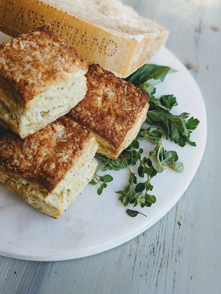 Three Parmesan Herb Biscuits on a plate with fresh herbs and a loaf of bread