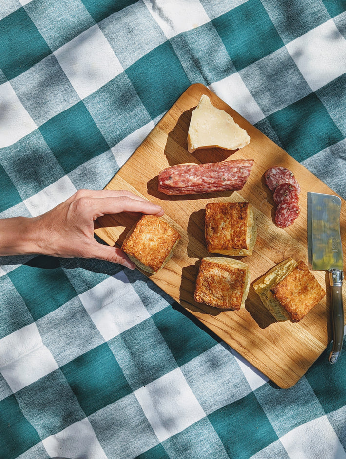 A hand reaching for Parmesan Herb Biscuits, salami, and cheese on a wooden board.