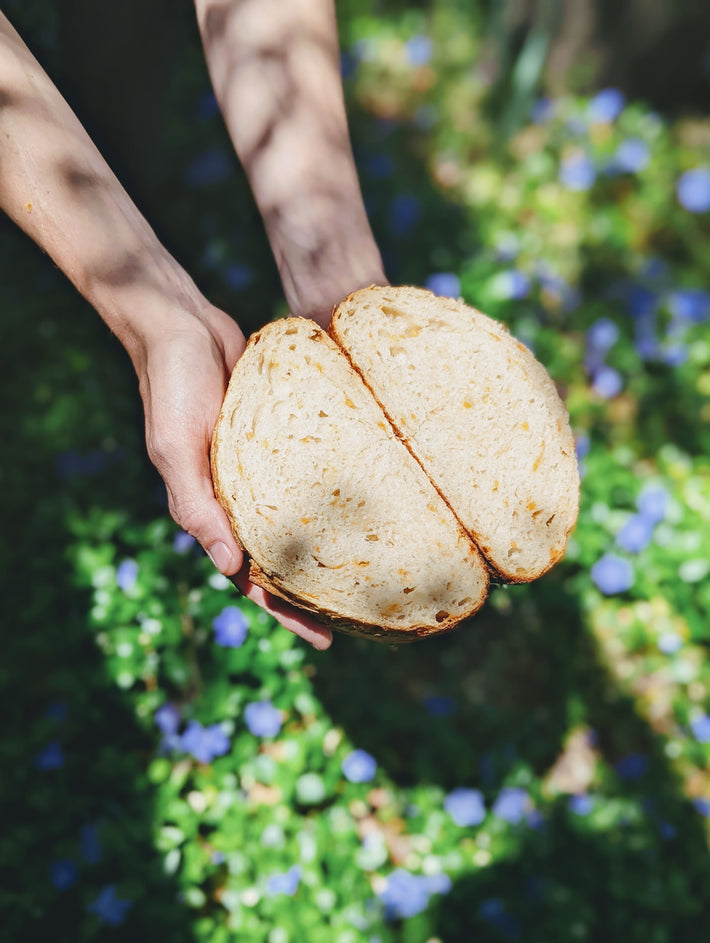 A person holding a loaf of sliced bread in a garden with flowers