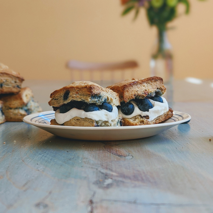 Two split scones filled with whipped cream and fresh blueberries on a plate on a wooden table