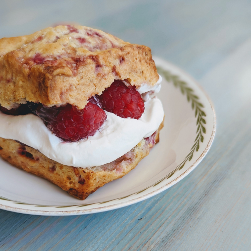 Raspberry scone split and filled with whipped cream and fresh raspberries on a white plate with green leaf border, close-up.