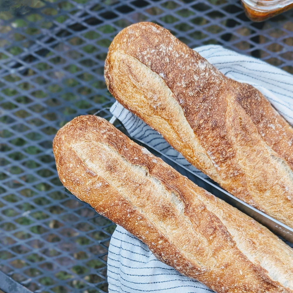 Two crusty baguettes on a striped cloth napkin on a metal patio table.