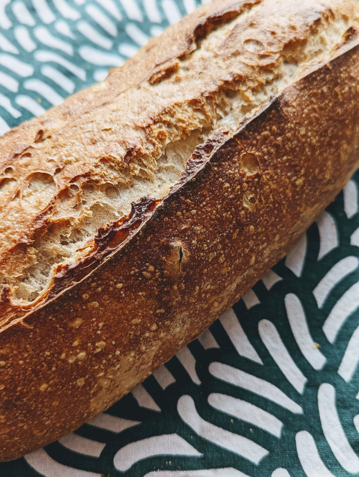 Crusty ancient spelt sourdough loaf on green-and-white patterned cloth