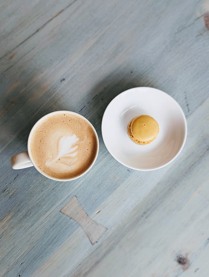 A cup of coffee with a macaron on a plate