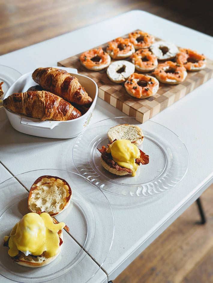 Croissants and bagels on a table, with eggs benedict in the foreground.