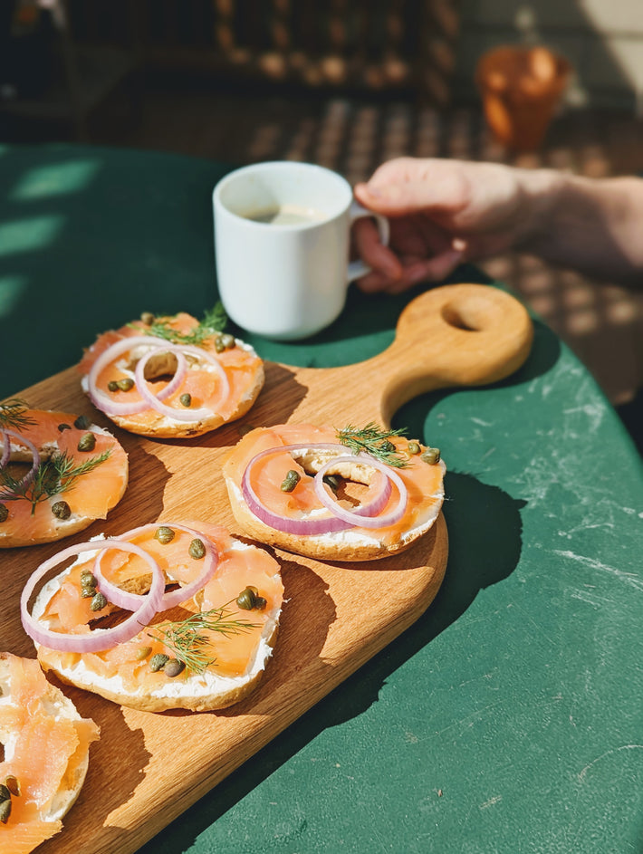 Bagels topped with smoked salmon, red onion, and capers on a wooden board with a cup of coffee