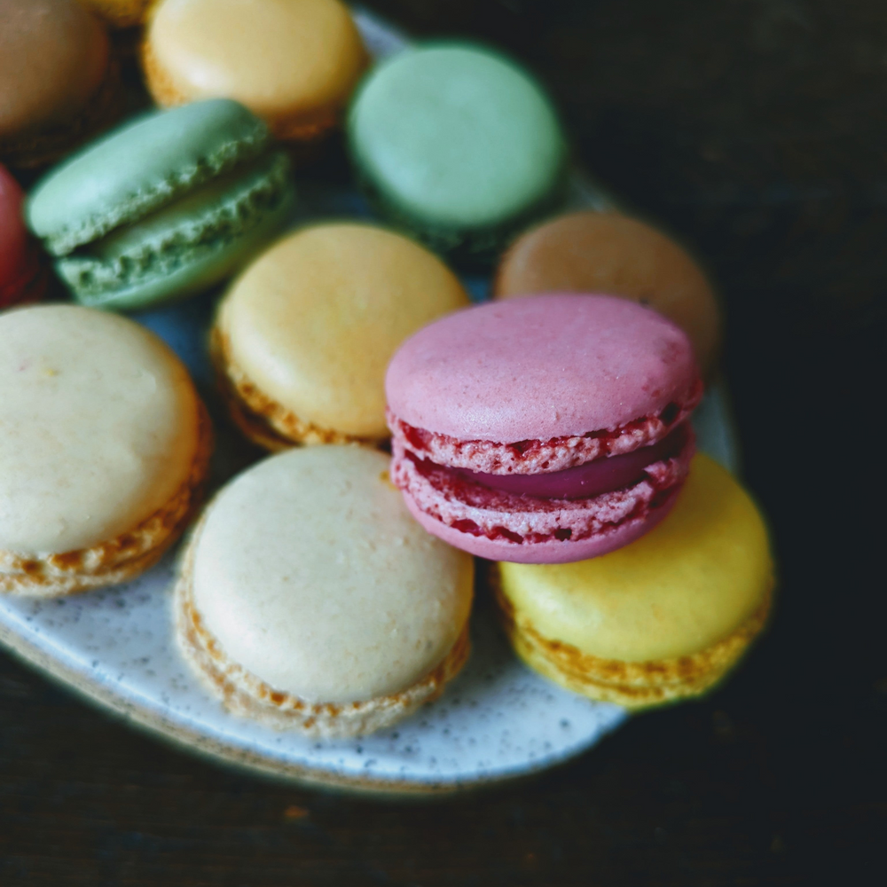 Assorted pastel macarons on a speckled ceramic plate against a dark background