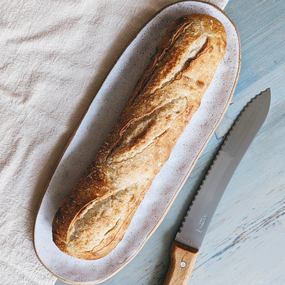 A Sourdough Demi Baguette on a plate with a knife beside it