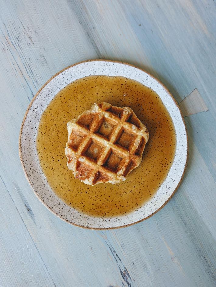 Belgian waffle centered on a speckled plate with syrup pooled around it on a light blue wooden table