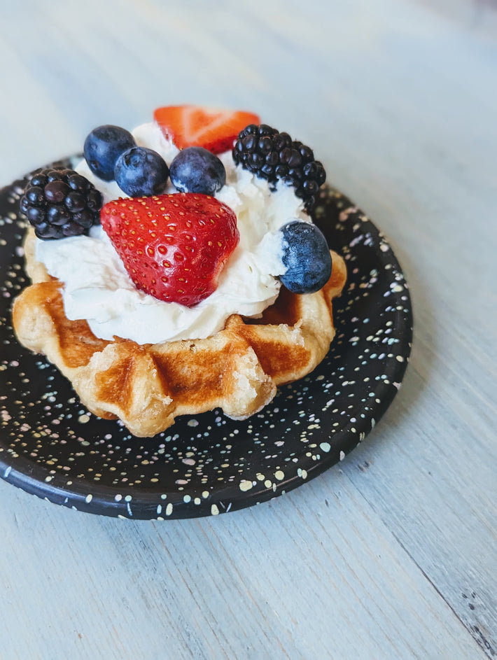 Belgian waffle topped with whipped cream, strawberries, blueberries, and blackberries