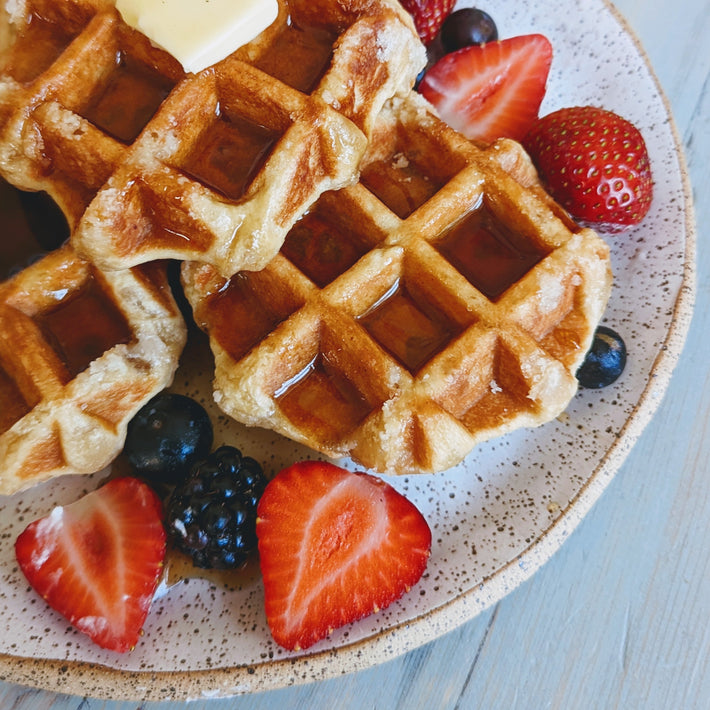Waffles with butter and syrup, served with strawberries, blueberries and blackberries on a speckled plate