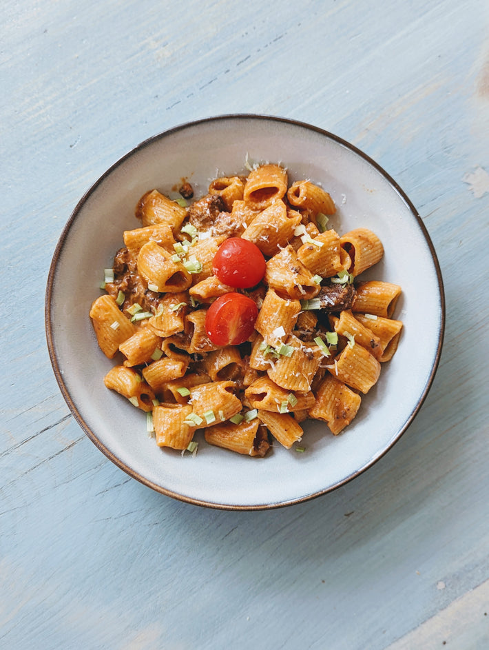 Rigatoni pasta with sauce, topped with cherry tomatoes and herbs