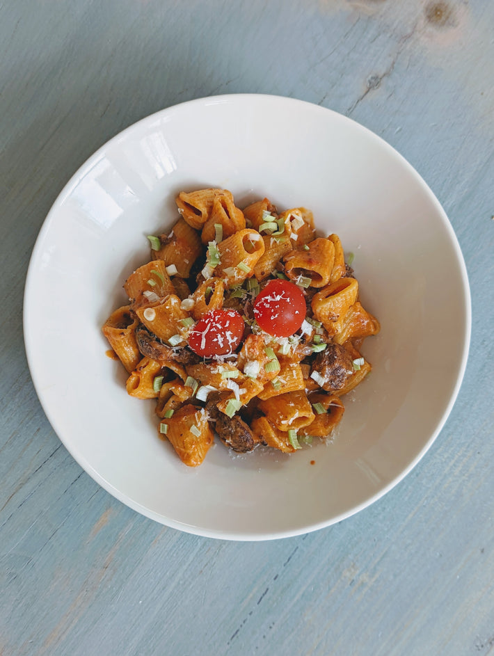 Rigatoni pasta with cherry tomatoes and herbs in a white bowl
