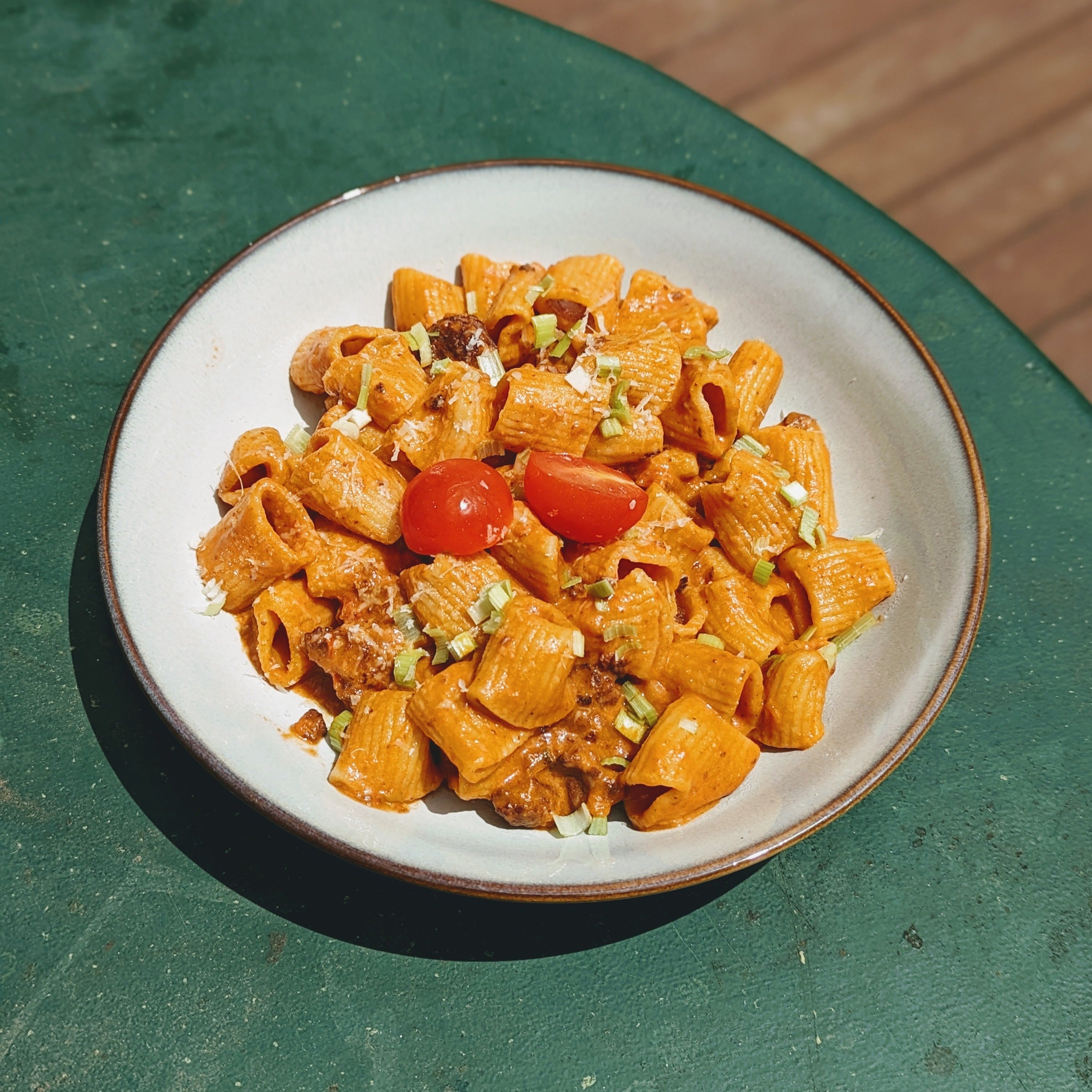 A plate of fresh rigatoni pasta with cherry tomatoes and green onions