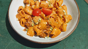 Rigatoni in tomato-and-sausage sauce with halved cherry tomatoes, grated cheese and chopped herbs on a ceramic plate