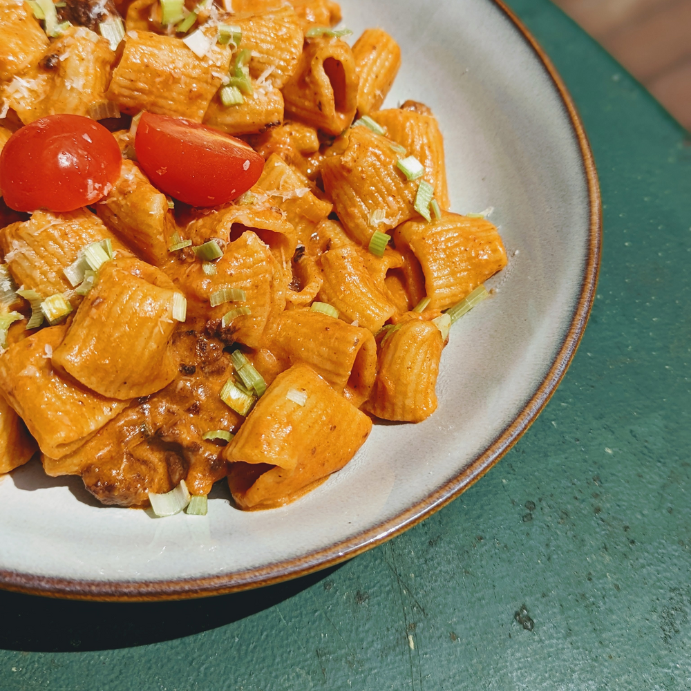 Creamy tomato rigatoni with sliced cherry tomatoes and chopped green onions on a gray-rimmed plate
