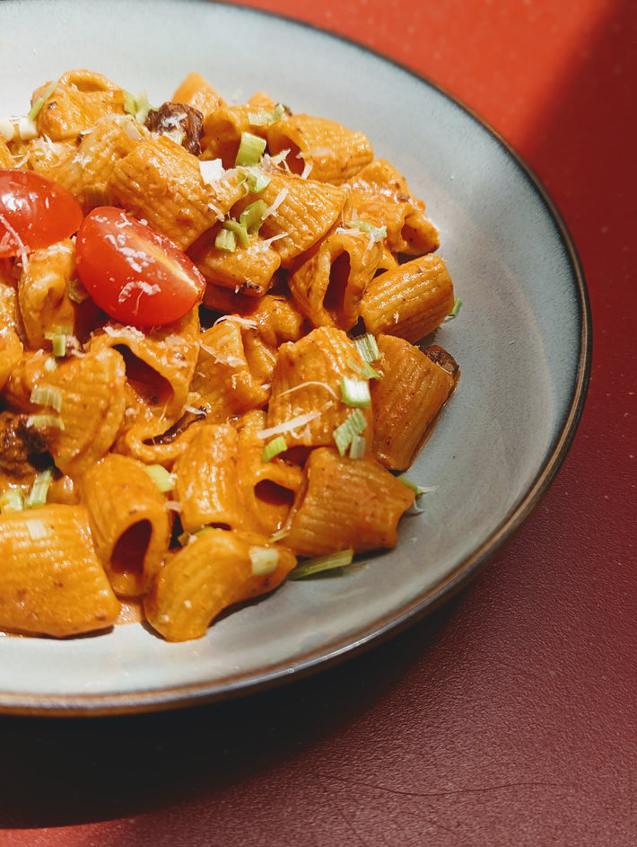 Plate of rigatoni pasta with cherry tomatoes and green onions
