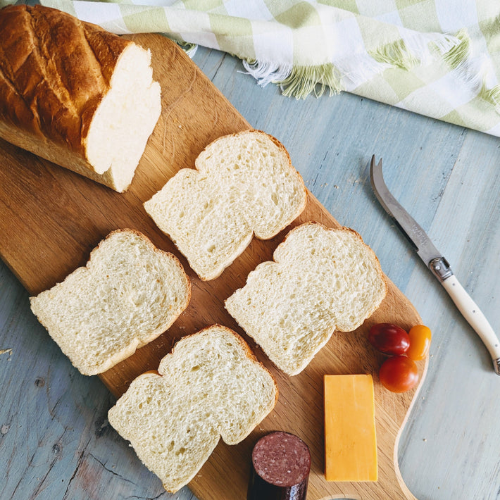 Sliced brioche bread on a cutting board with cheese, tomatoes, and salami