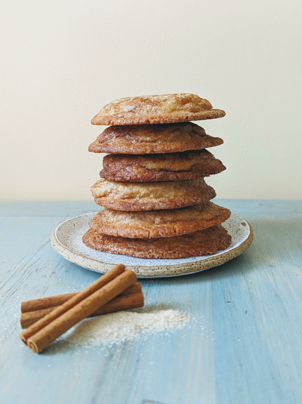 A stack of Snickerdoodle cookies on a plate with cinnamon sticks