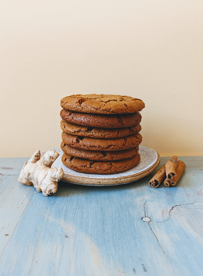 Giant Ginger Molasses Cookies stacked on a plate with ginger and cinnamon sticks