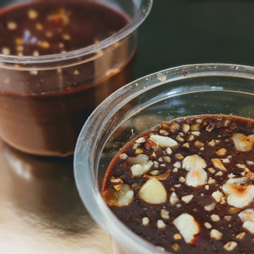 Two clear plastic cups with chocolate pudding topped with chopped hazelnuts.