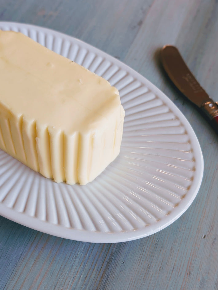 Stick of butter with ridged sides on a white fluted plate beside a butter knife.