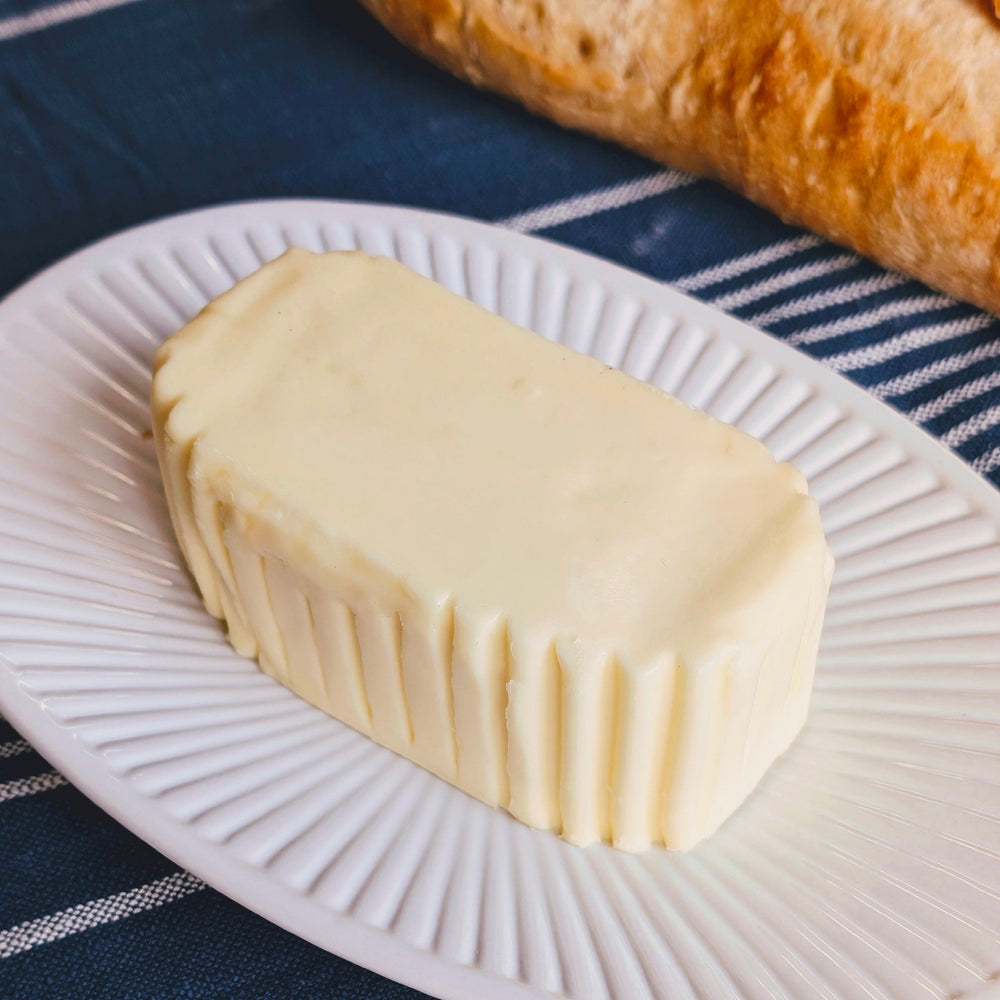 Rectangular molded butter with ridged sides on a white plate, baguette in background and a LAGUIOLE Jean Dubost butter knife.