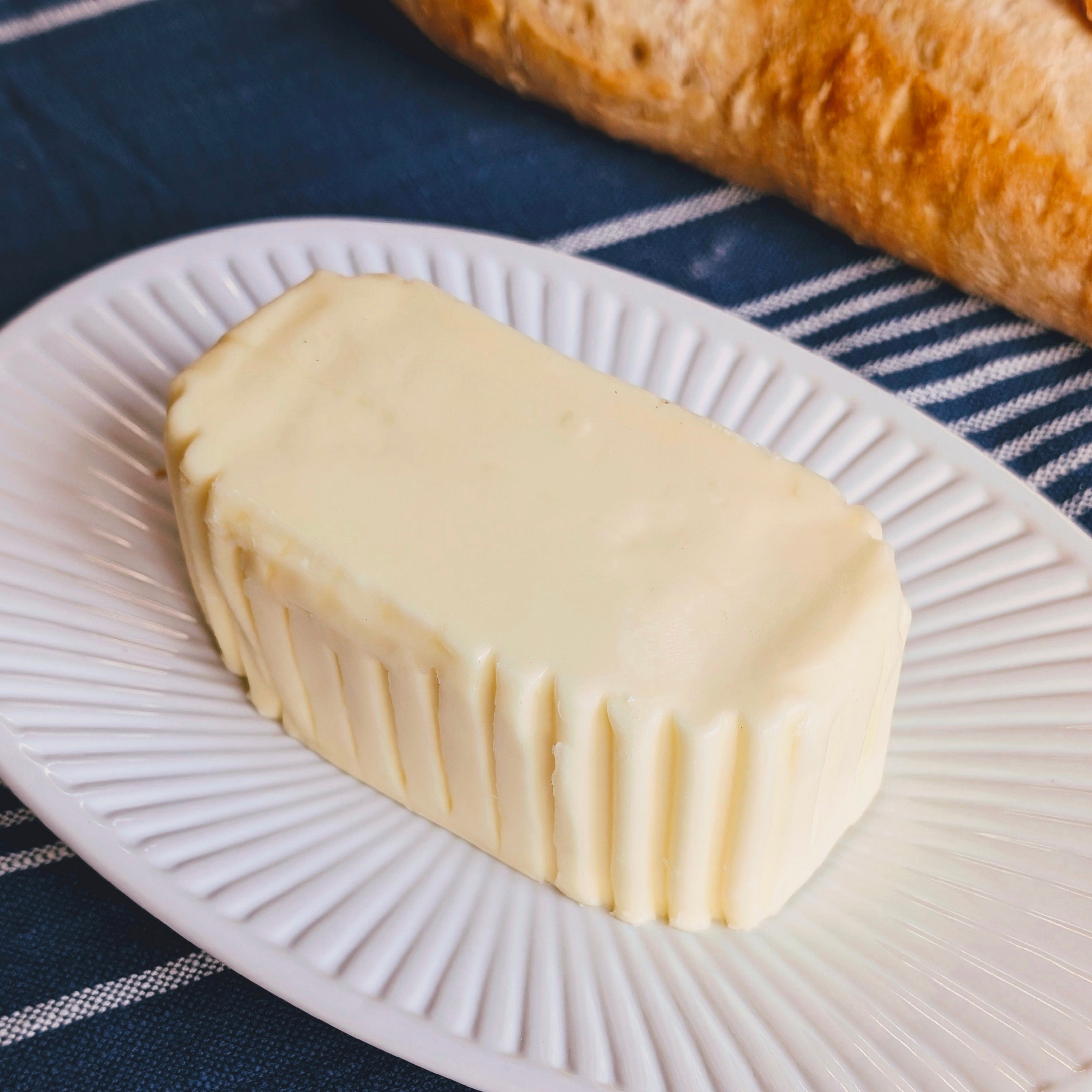 Rectangular molded butter with ridged sides on a white plate, baguette in background and a LAGUIOLE Jean Dubost butter knife.