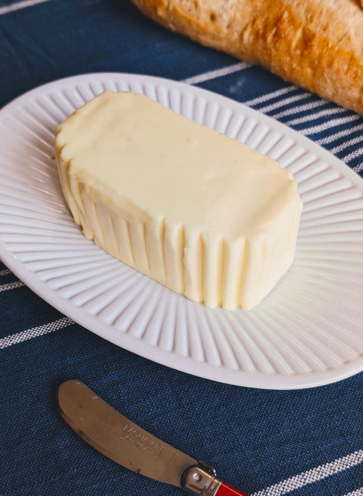 Rectangular molded butter with ridged sides on a white plate, baguette in background and a LAGUIOLE Jean Dubost butter knife.