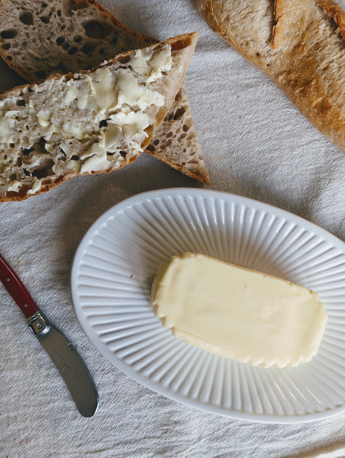 A plate with a block of butter and slices of bread spread with butter.