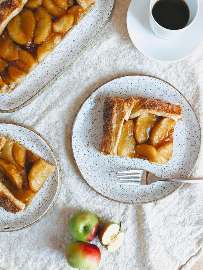 Slice of apple caramel galette on a plate with a fork and coffee