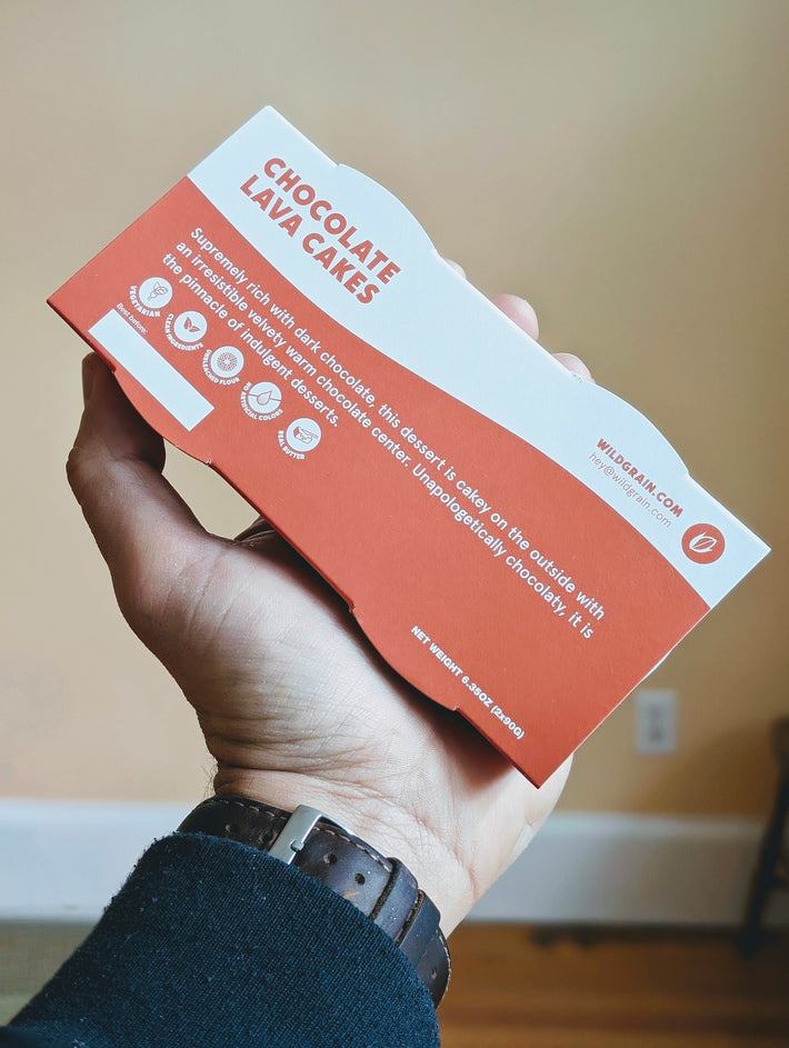 Chocolate Lava Cakes box in hand showing text: CHOCOLATE LAVA CAKES; WILDGRAIN.COM; hey@wildgrain.com; NET WEIGHT 6.35OZ (2x90G)