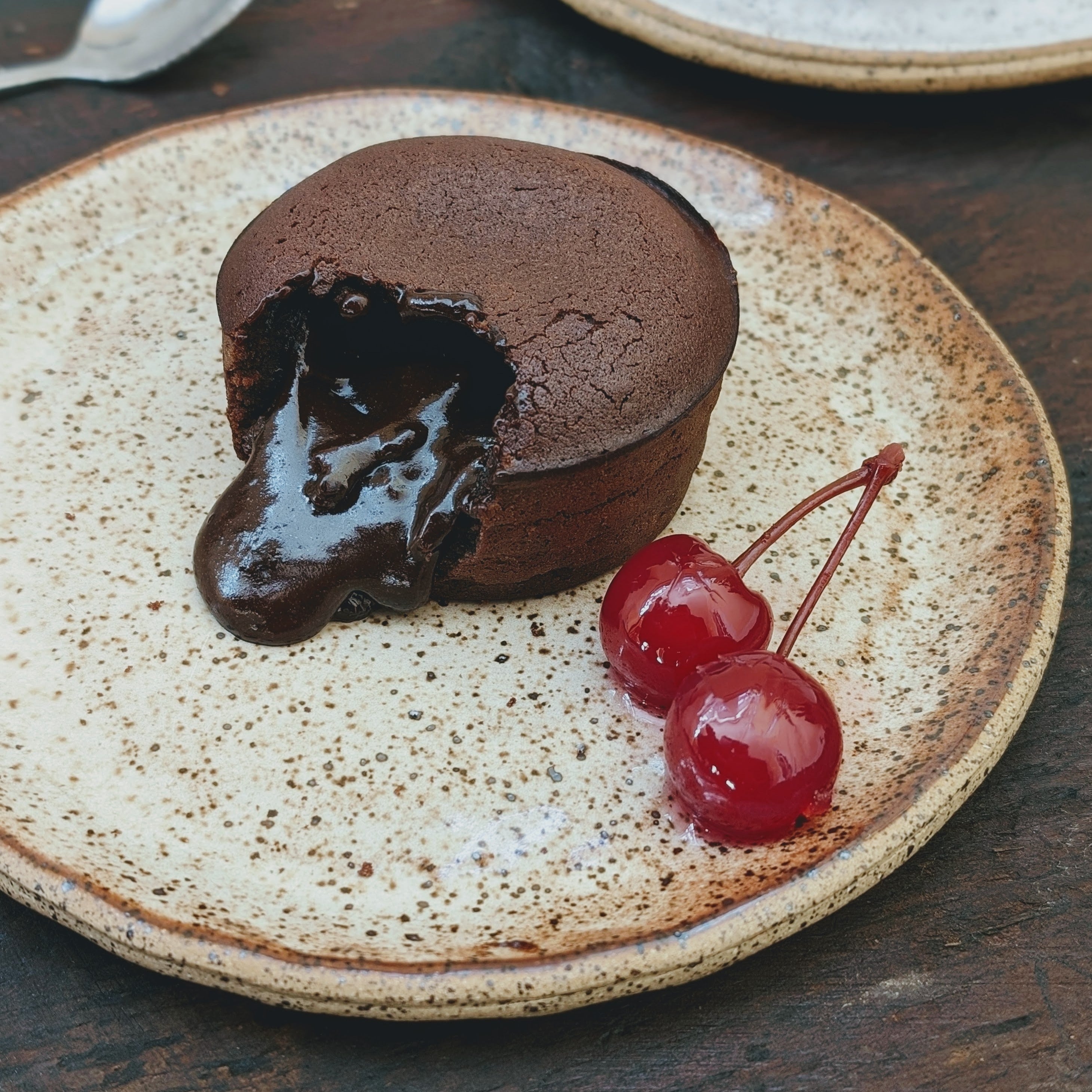 chocolate molten lava cake with oozing ganache served with two maraschino cherries on a speckled ceramic plate