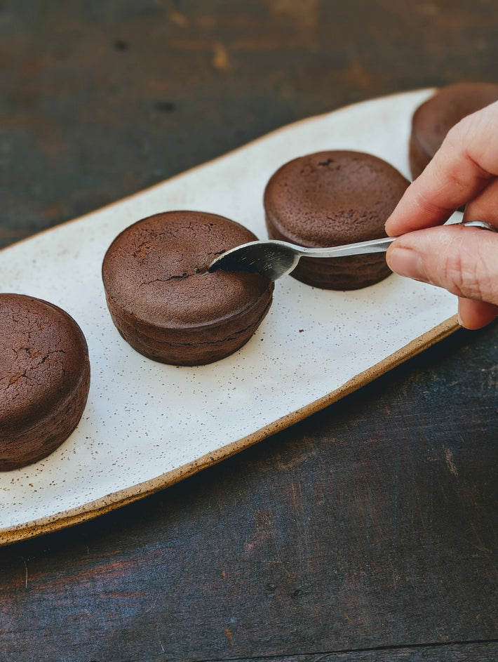 A hand holding a spoon over a chocolate lava cake on a plate