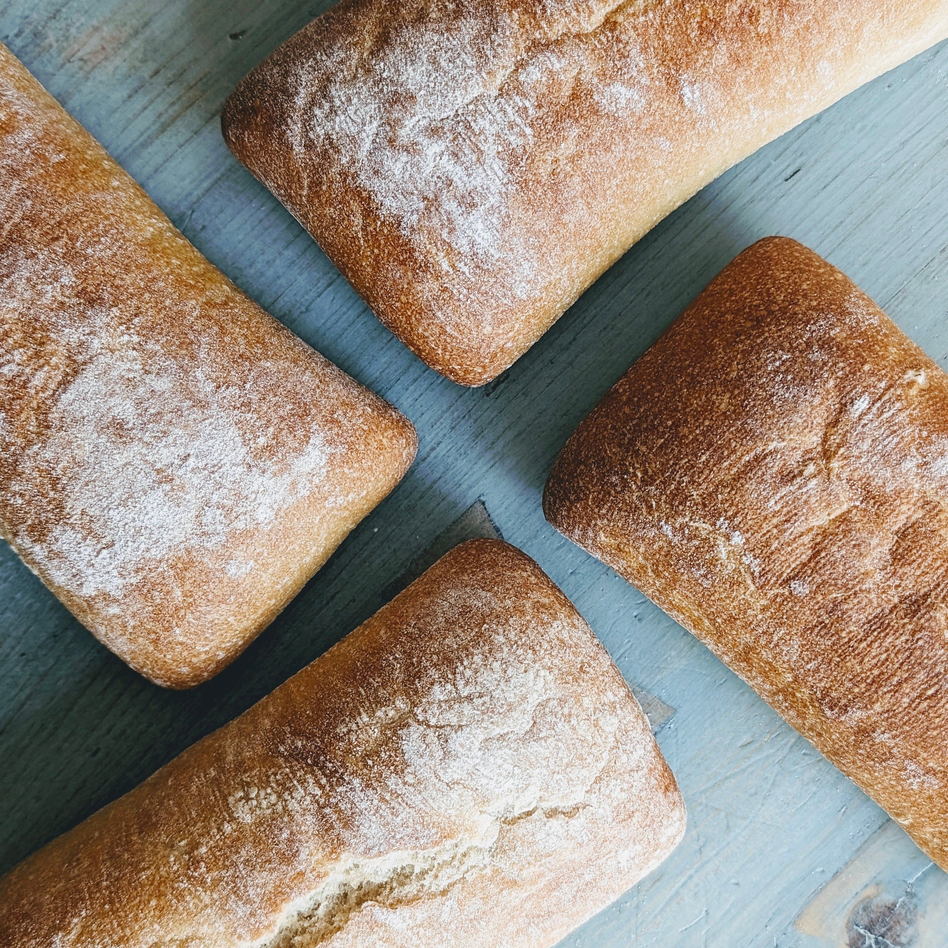 Four ciabatta loaves dusted with flour on a wooden board, top-down view
