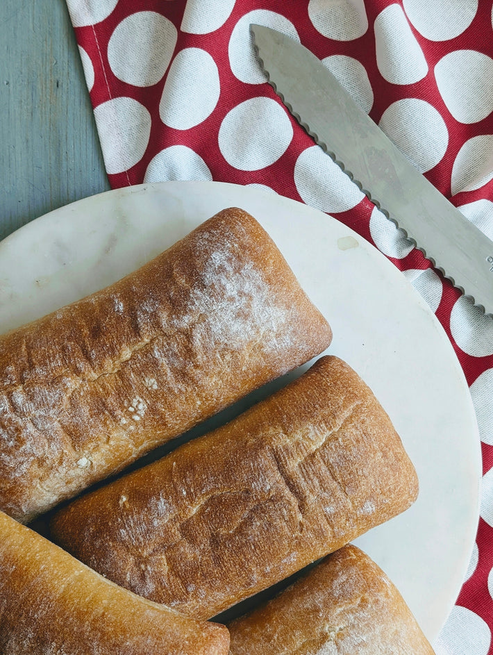 Slow-fermented ciabatta rolls on a plate with a knife and red polka dot cloth